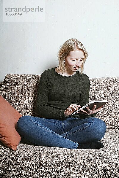 Junge Frau sitzt auf der Couch und entspannt sich zu Hause mit einem Tablet-Computer