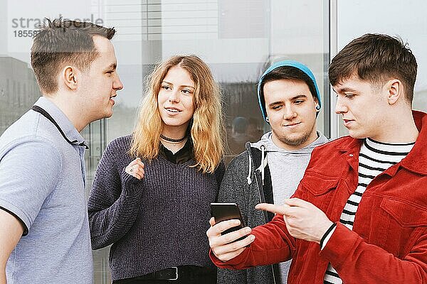 Eine Gruppe von Freunden im Teenageralter unterhält sich oder diskutiert  der junge Mann zeigt etwas auf seinem Smartphone