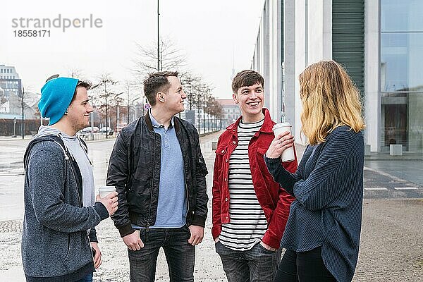 Gruppe junger erwachsener Freunde  die sich unterhalten  während sie mit Coffee-to-go-Bechern auf einer Straße in Berlin zusammenstehen