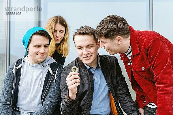 Junger Mann zeigt Bitcoin-Münze zu seiner faszinierten Gruppe von Freunden  Kryptowährung Hype-Konzept
