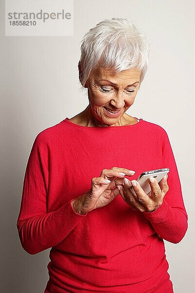 Glückliche ältere Frau mit Smartphone beim Tippen einer Textnachricht