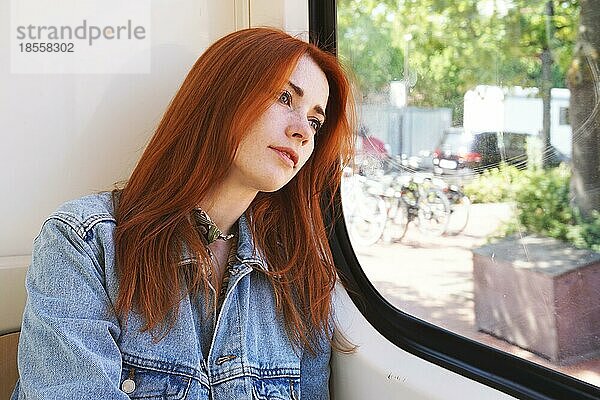 Candid junge Frau sitzt in Straßenbahn oder Straßenbahn Blick aus dem Fenster - öffentliche Verkehrsmittel und Pendeln Konzept