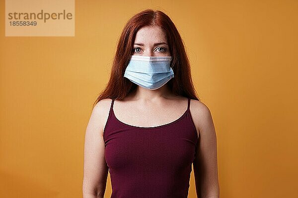 Junge Frau trägt eine medizinische Gesichtsmaske  die Mund und Nase bedeckt - Schutz gegen Corona-Virus - Studio-Porträt auf orangefarbenem Hintergrund mit Kopierraum