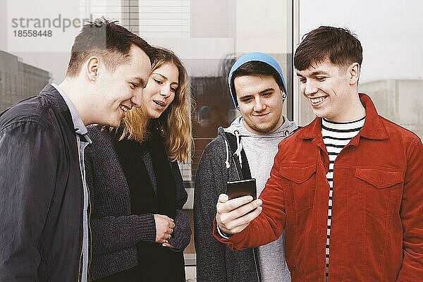 Junger Mann zeigt einer Gruppe von Freunden etwas Lustiges auf seinem Smartphone - urbane Teenager  die Spaß haben und zusammen lachen