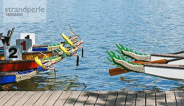 Drachenboote  die an einem Holzsteg oder einer Mole am See festgemacht sind