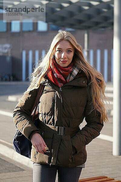 Straße Stil Mode Porträt der jungen Frau wartet am Busbahnhof an einem sonnigen Tag im Winter