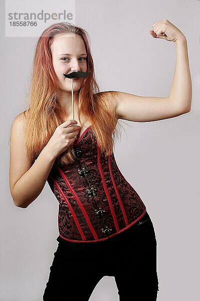 Junge Frau mit falschem Schnurrbart auf einem Stock  die ihre Bizepsmuskeln zeigt