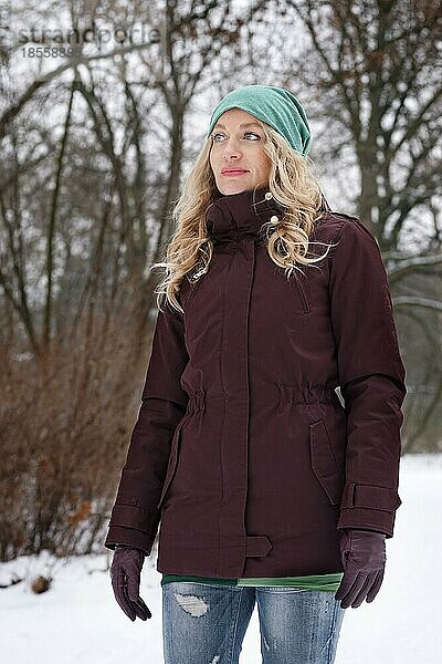 Blonde Frau im verschneiten Wald im Winter stehend