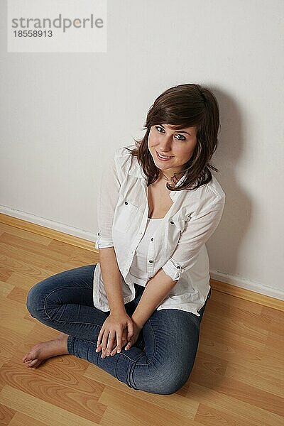Lächelnde junge Frau im Schneidersitz auf dem Boden sitzend