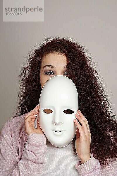Schüchterne junge Frau nimmt schlichte weiße Maske ab