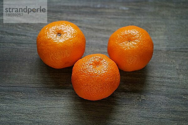 Drei ganze Clementinen oder Mandarinen auf einem rustikalen Holztisch mit geringer Tiefenschärfe