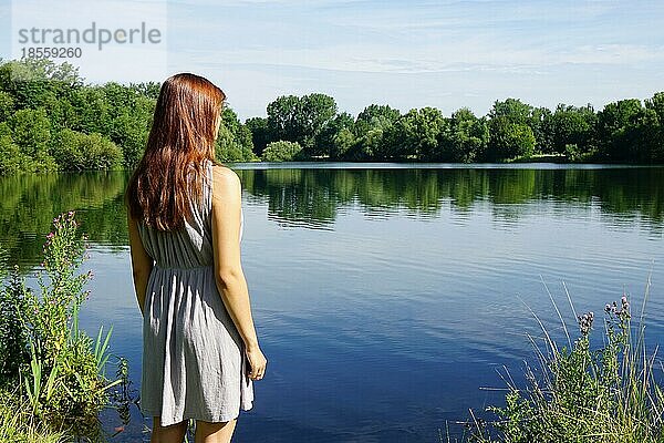 Rückansicht einer jungen Frau mit Blick auf einen idyllischen See mit Kopierraum