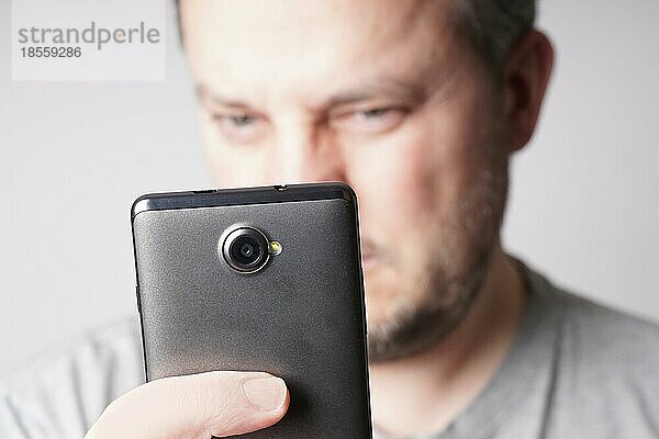 Mann mittleren Alters schaut auf sein Smartphone oder macht ein Selfie. geringe Tiefenschärfe