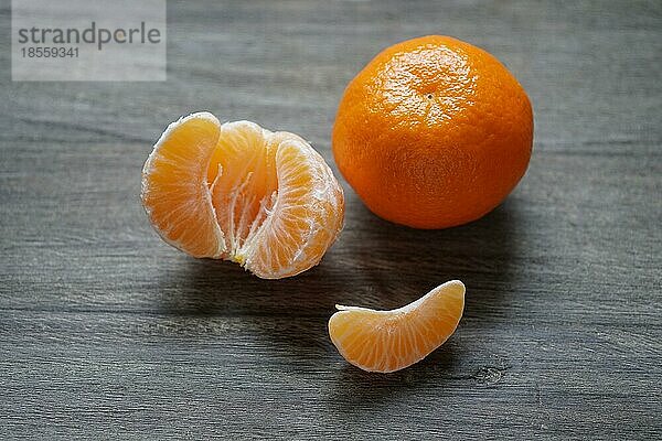 Geschälte und ungeschälte Clementinen oder Mandarinen auf rustikalem Holzbrett mit geringer Tiefenschärfe
