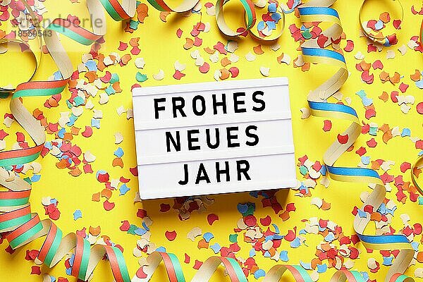 Frohes neues Jahr bedeutet frohes neues Jahr auf Deutsch - Party Feier flach legen mit Konfetti und Luftschlangen auf gelbem Hintergrund