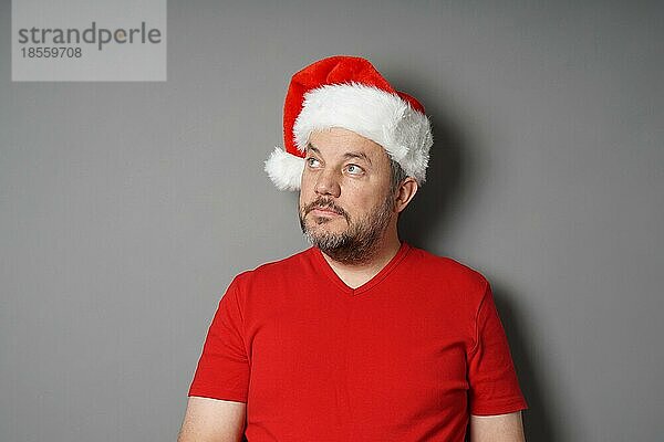 Mitte erwachsenen Mann trägt Weihnachtsmann Hut und rotes T-Shirt Blick nach oben zu kopieren Raum - echte Menschen Weihnachten Konzept