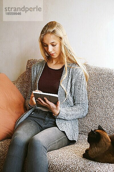 Teenager-Mädchen mit Tablet-Computer zu Hause beim Entspannen auf dem Sofa mit Katze - offen echte Menschen Lebensstil
