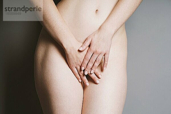 Mittelteil einer unkenntlichen jungen nackten Frau  die ihre Geschlechtsteile oder ihren Genitalbereich mit den Händen bedeckt
