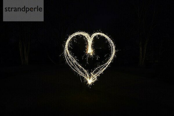Herzförmige Lichtmalerei mit Wunderkerzen im Freien bei Nacht - Symbol für Liebe und Romantik