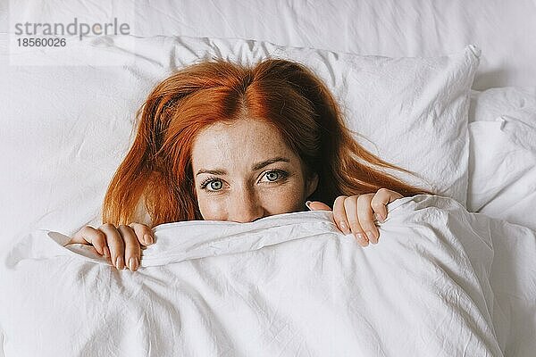 Schüchterne junge Frau  die sich unter der Bettdecke versteckt und schüchtern wirkt
