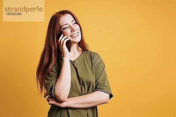 Fröhlich lachende junge Frau  die auf ihrem Smartphone oder Handy spricht - gelber Hintergrund mit Kopierraum