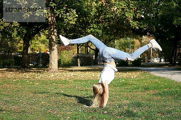 Unbekümmerte junge Frau  die im Park einen spontanen Handstand macht