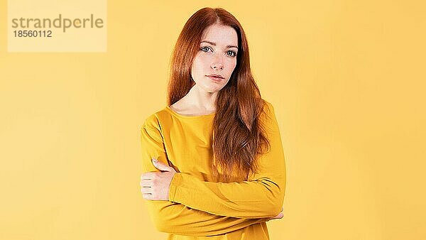 Studio-Porträt einer ernsten jungen Frau mit verschränkten Armen - gelber Hintergrund mit Leerzeichen
