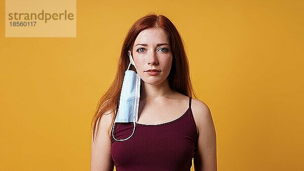 Junge Frau mit medizinischer Gesichtsmaske  die an ihrem Ohr hängt - unsachgemäße Verwendung der Corona-Coronavirus-Schutzmaske
