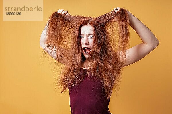 Frustrierte junge Frau  die an ihren langen roten Haaren zieht und reißt  wenn sie einen schlechten Tag hat