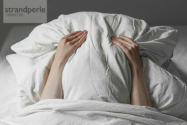 Unerkennbare Frau im Bett  die ihr Gesicht unter dem Kissen versteckt  um sich vor dem Sonnenlicht am frühen Morgen zu schützen