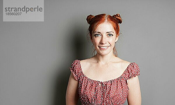 Glückliche junge Frau mit großem Lächeln und roten Haaren Raum Brötchen auf grauem Hintergrund mit Kopie Raum