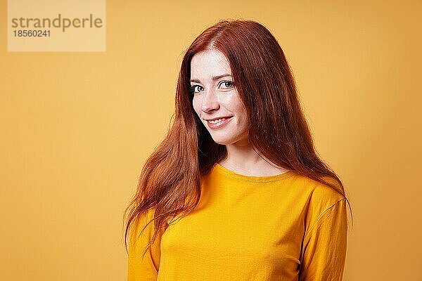 Glückliche junge Frau mit langen roten Haaren lächelnd - gelber farbiger Hintergrund mit Kopierraum