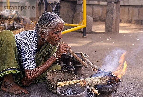 Eine alte Frau verbrennt Holz mit einem Windrohr in Kokkarebellur  Karnataka  Südindien  Indien  Asien