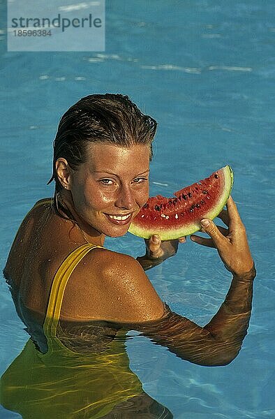 Junge Frau ißt Melone im am swimmingpool  erfrischung im Sommer  Sommerhitze  Wassermelone (Citrullus lanatus)