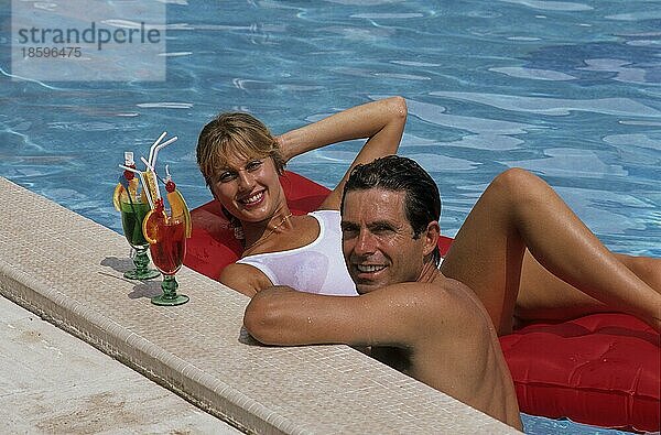 Junges Paar am Pool  Frau liegt auf Luftmatratze Mann am Beckenrand  mit Cocktail