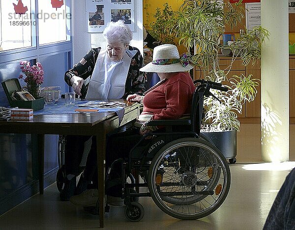Zwei alte Frauen mit Rollstuhl beim Zeitung lesen im Pflegeheim  Altenheim