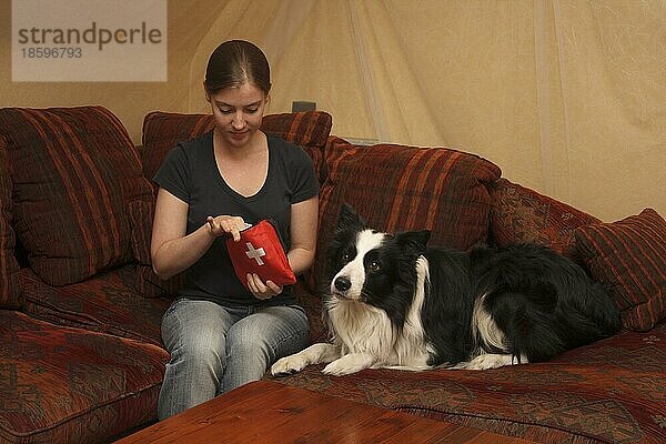 Junge Frau sitzt mit Border Collie auf der Couch und hat Erste Hilfe Set für Hunde in der Hand