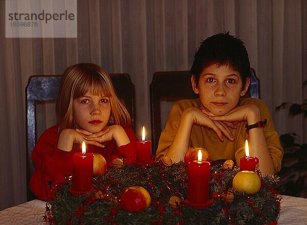 2 zwei Kinder sitzen am Adventskranz  4 vier brennende Kerzen  Weihnachtszeit  Advent  2 two children sit in the Advent wreath  4 four burning candles  yule tide