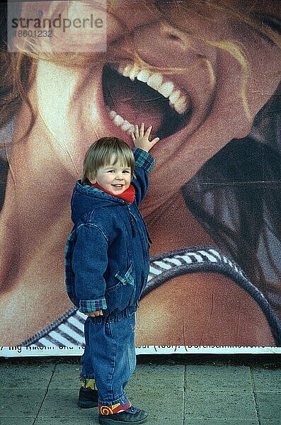 Kleines Kind vor einer Werbung mit lachender Frau  Bayern  Deutschland  Europa