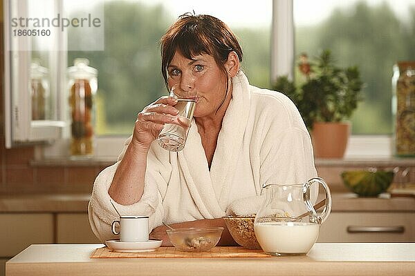 Frau beim Frühstück trinkt Glas Wasser  Frühstück  frühstücken  Kanne Milch  Schüsseln  Müsli  Tasse Kaffee  frühstückt