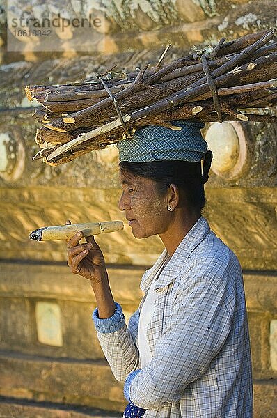 Burmesin trägt Holz auf Kopf und raucht traditionelle Zigarre  Bagan  Burma  Myanmar  Cheroot  Sheroot  Asien
