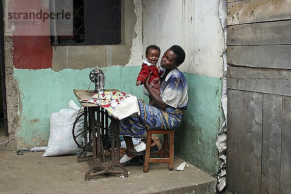 Näherin mit Kind bei der Arbeit mit alter Usha-Tretnähmaschine zu Hause  Ruhengeri  Musanze  Ruanda  Zentralafrika  Afrika