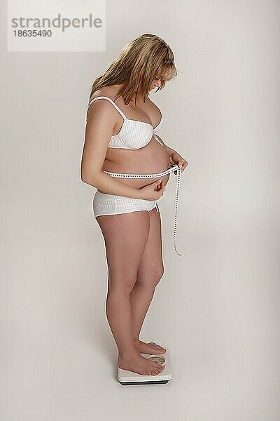 Schwangere Frau auf Waage mit Maßband  wiegen  Gewicht  seitlich  Personenwaage  Zentimetermaß  messen  Umfang  Bauchumfang  nachmessen  mißt  Freisteller  freistellbar