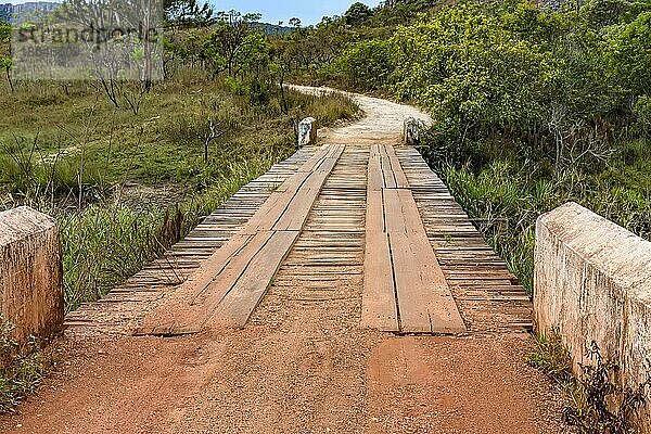 Schotterstraße mit rustikaler und primitiver Holzbrücke zwischen Hügeln und der Vegetation des Naturschutzgebiets Biribiri in Diamantina  Brasilien  Südamerika