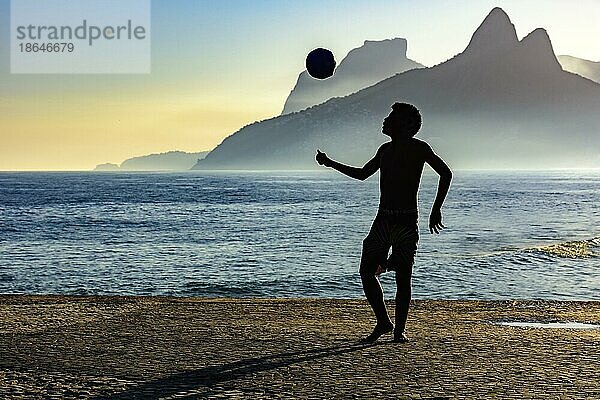 Junge spielt Fußball vor dem Meer und den Hügeln bei Sonnenuntergang  Ipanema  Rio de Janeiro  Rio de Janeiro  Brasilien  Südamerika