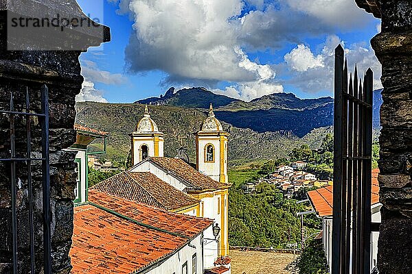 Schöne historische Kirche in der Stadt Ouro Preto  gesehen zwischen alten Steinportalen mit den Bergen im Hintergrund  Brasilien  Südamerika