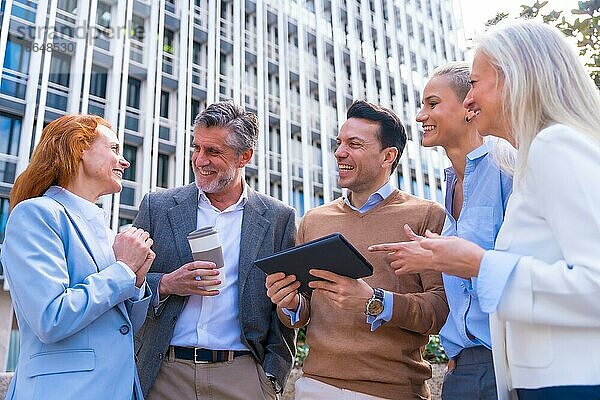 Fröhliche Gruppe von Mitarbeitern  die lachen und auf ein Tablet im Freien in einem Bürogebäude schauen  Geschäftsfrau und Geschäftsmann und Führungskräfte im kommerziellen Bereich