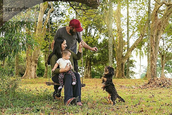 Glückliche Familie  Vater und Mutter lächelnd und Blick auf ihr Baby  im Freien und spielen mit ihrem Welpen