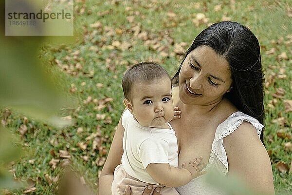 Porträt einer attraktiven hispanischen Mutter mit ihrem Baby in einem Park. Baby schaut in die Kamera