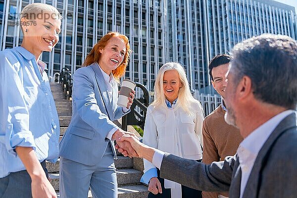Begrüßung und Händeschütteln eines Mitarbeiters. Gruppe von Führungskräften oder Geschäftsleuten im Freien in einem Bürobereich